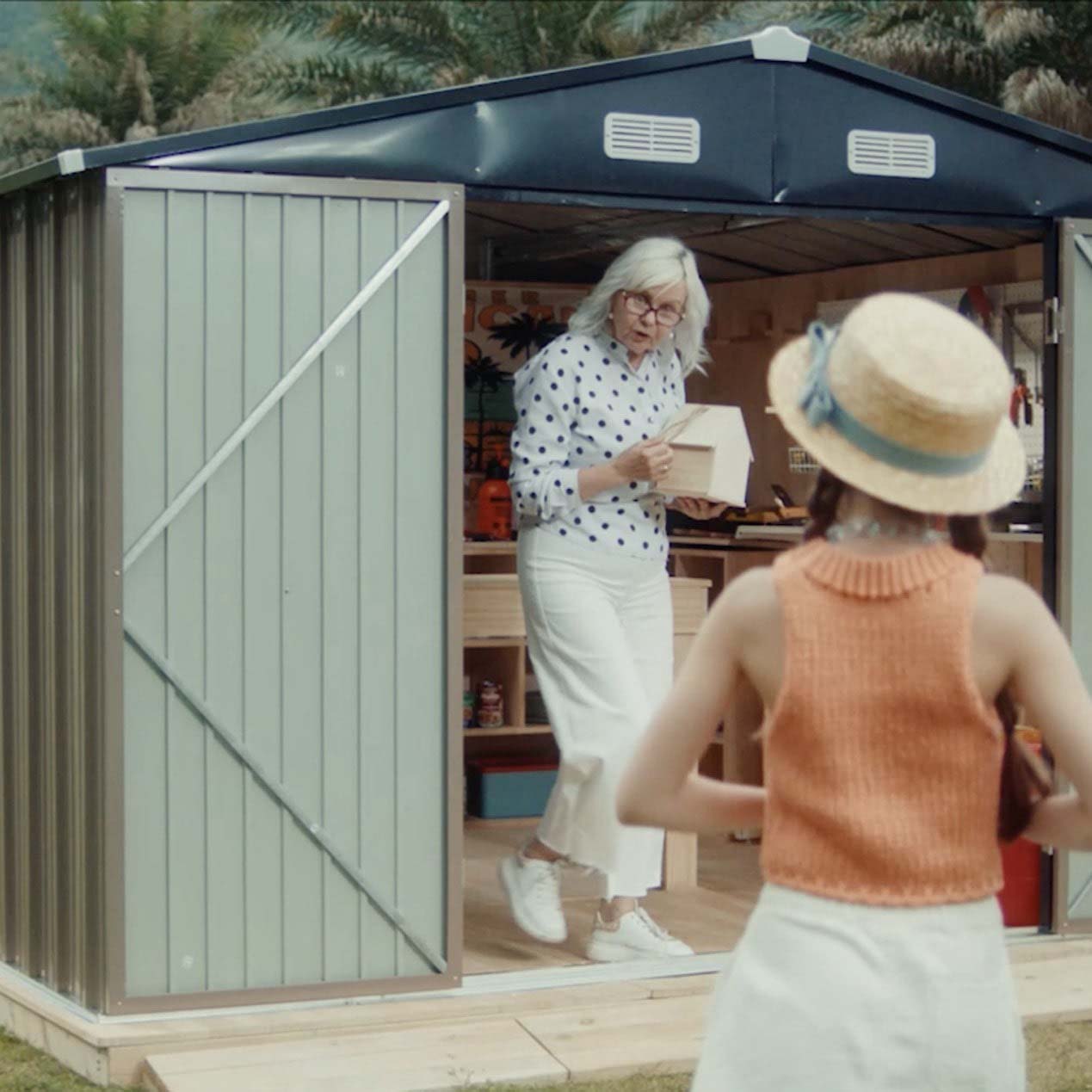 Grandma stands inside the metal storage shed, talking to her granddaughter outside.