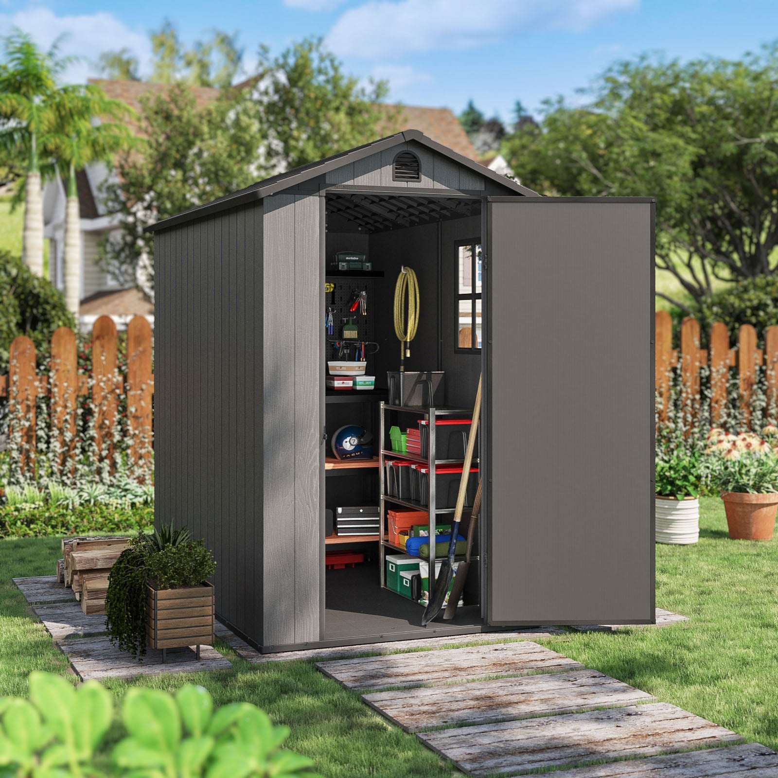 Gray metal storage shed with tools and items on a grassy area with a wooden fence and trees in the background.