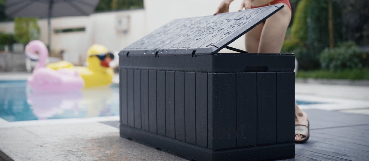 A lady is opening the lid of a outdoor storage box that got wet by the poolside