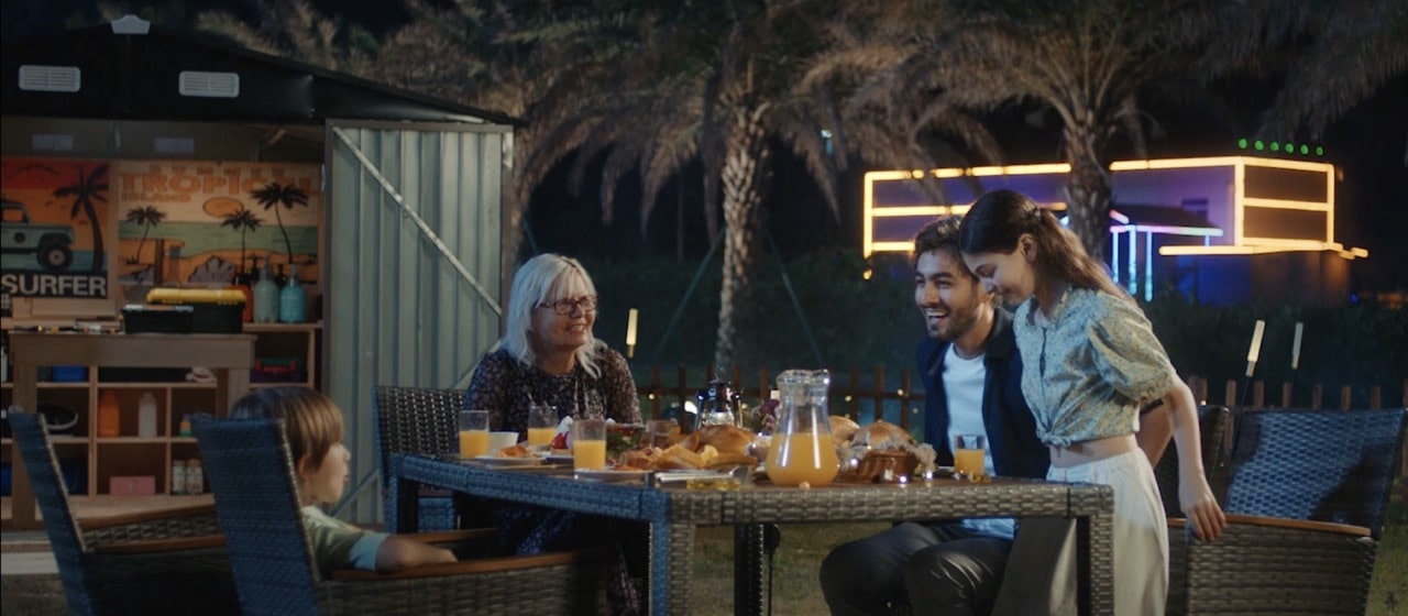 A family having dinner at the table outside the metal storage shed.