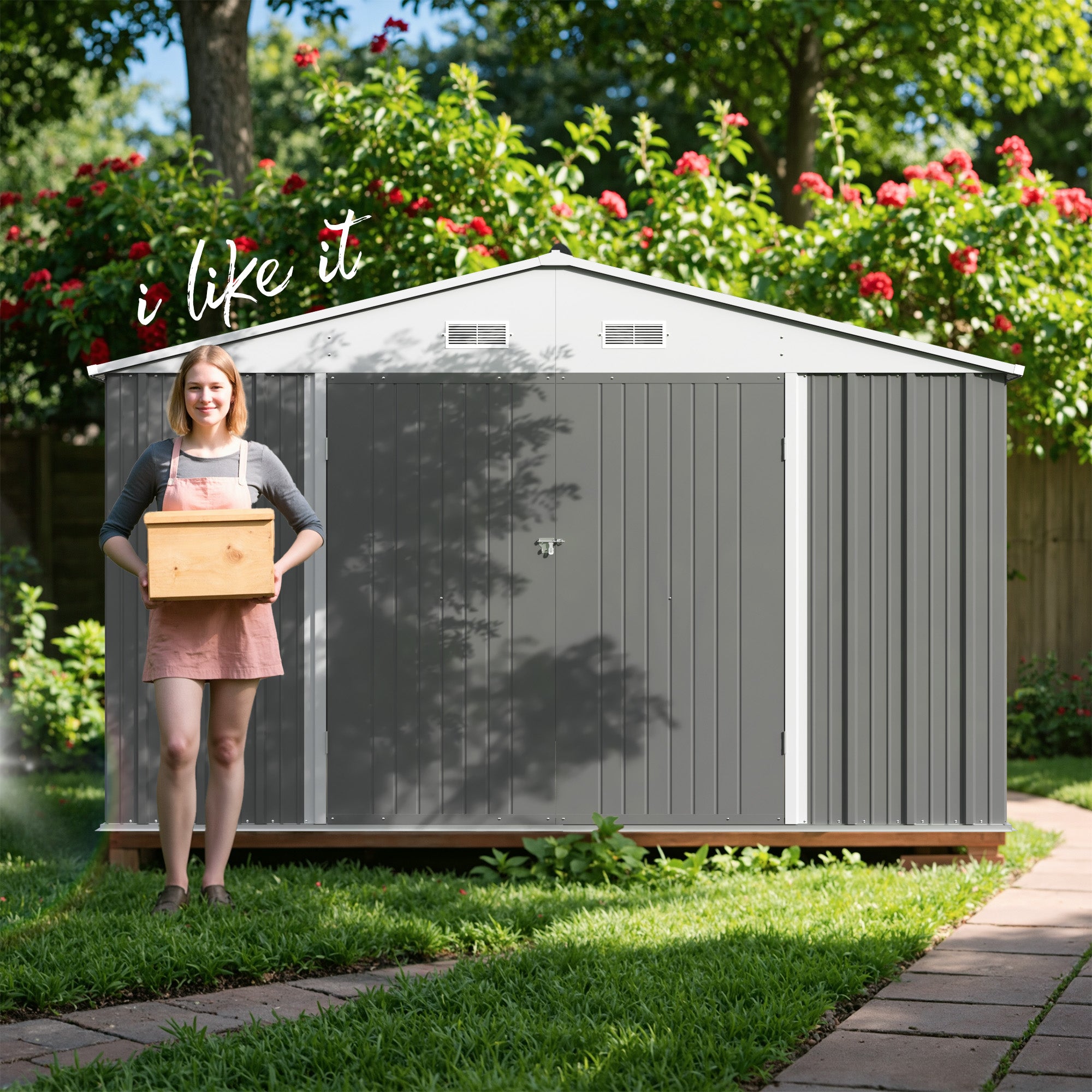 Woman holding a box in front of a gray storage shed with greenery and flowers in the background.