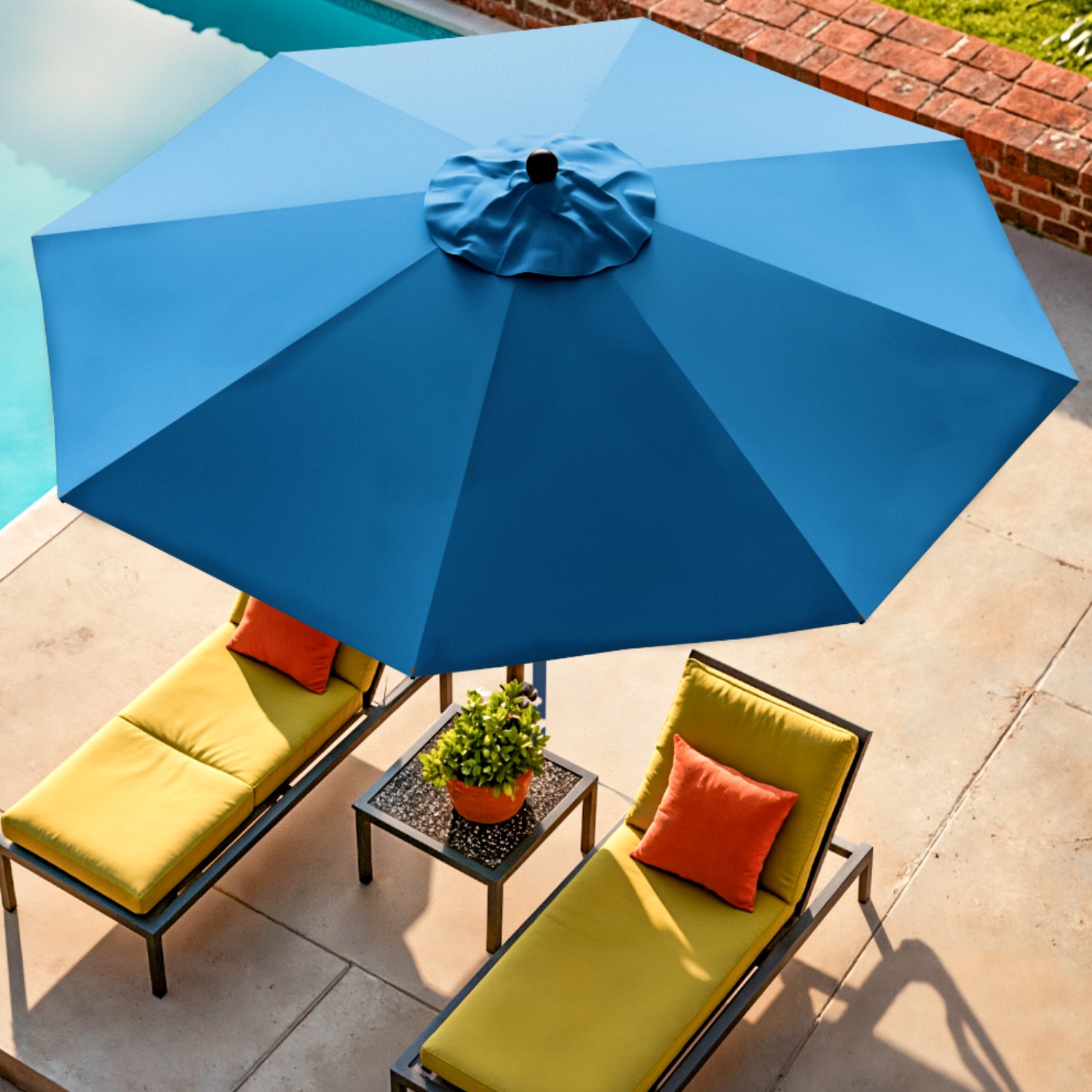 Blue patio umbrella over yellow lounge chairs with red cushions on a patio.